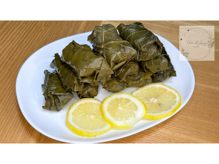 A plate of homemade Dolma (stuffed grape leaves), tightly rolled and packed with flavorful filling, garnished with fresh lemon slices and olive oil.
