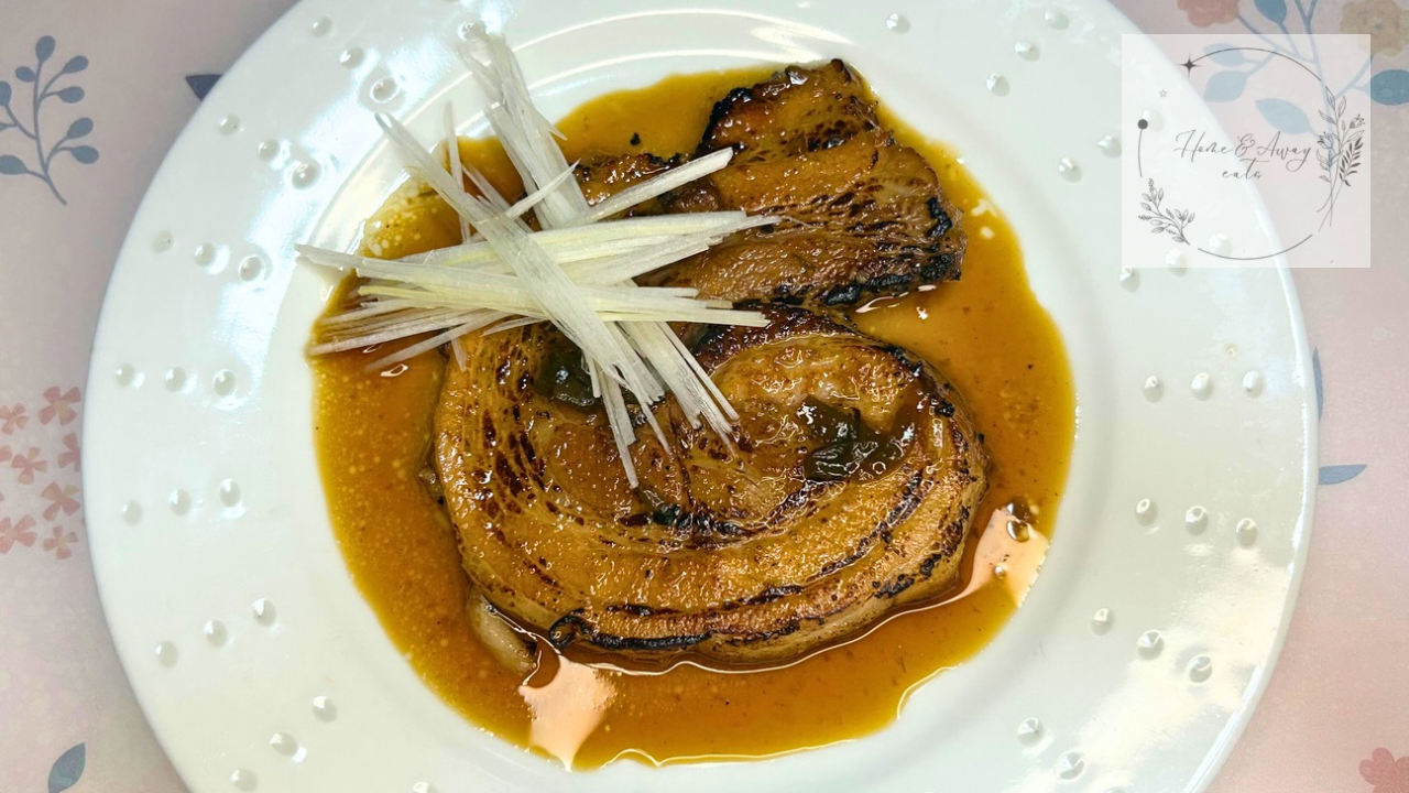 Sliced pork belly chashu after torching, drizzled with glossy sauce and topped with fine shredded white scallions.