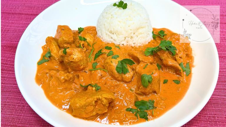 A plate of butter chicken curry served with steamed white rice and topped with Italian parsley