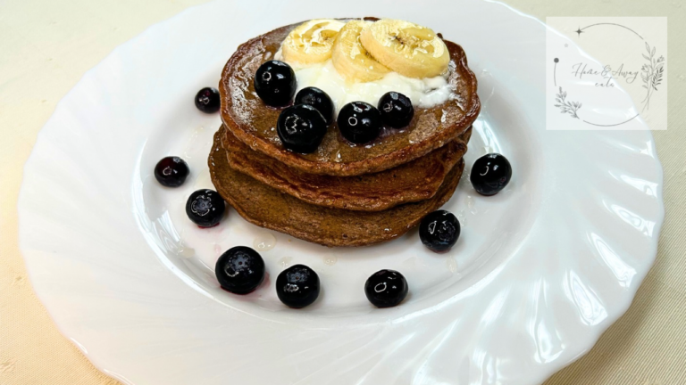 Protein pancakes topped with banana slices, yogurt, and blueberries on a white plate