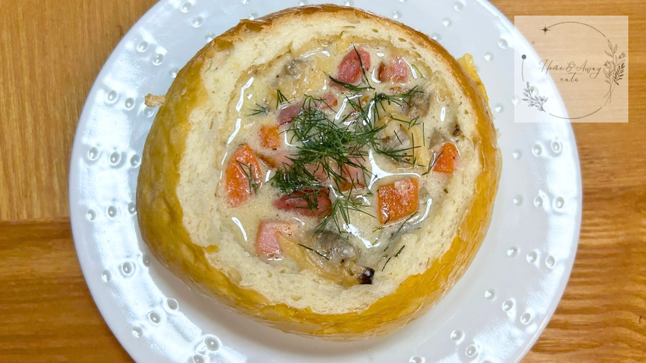 Creamy clam chowder served inside a bread bowl with crispy bacon and fresh herbs on top